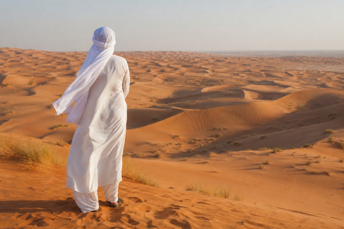 A woman in a headscarf standing in the Wahiba Sands desert after letting her tyres down in Bidiyah